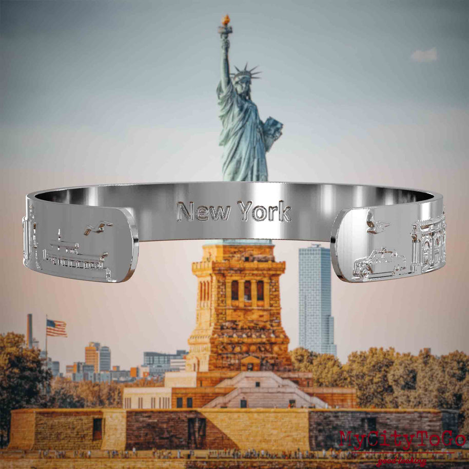 Innenseite eines silbernen Armreifs mit Reliefs bekannter Sehenswürdigkeiten der Stadt New York und einer Gravur des Stadtnamens. Den Hintergrund bildet eine Ansicht der Stadt New York.