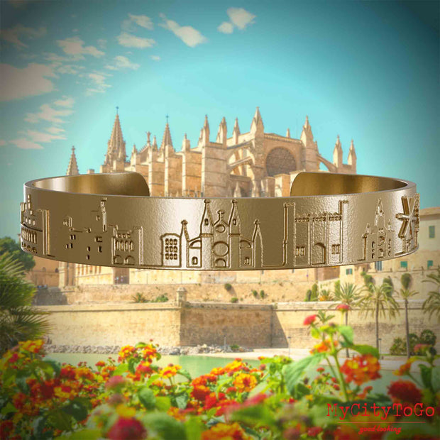 Armreif aus vergoldetem Edelstahl mit Reliefs bekannter Sehenswürdigkeiten der Stadt Palma de Mallorca. Den Hintergrund bildet eine Ansicht der Stadt Palma de Mallorca.