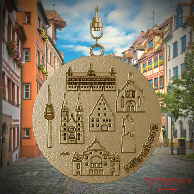Halskette mit Drehwirbel und Vorderseite eines Schmuckanhängers aus vergoldetem Edelstahl, auf dem Reliefs bekannter Sehenswürdigkeiten der Stadt Nuernberg abgebildet sind. Den Hintergrund bildet eine Ansicht der Stadt Nuernberg.