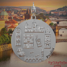 Halskette mit Drehwirbel und Vorderseite eines silbernen Schmuckanhängers, auf dem Reliefs bekannter Sehenswürdigkeiten der Stadt Prag abgebildet sind. Den Hintergrund bildet eine Ansicht der Stadt Prag.
