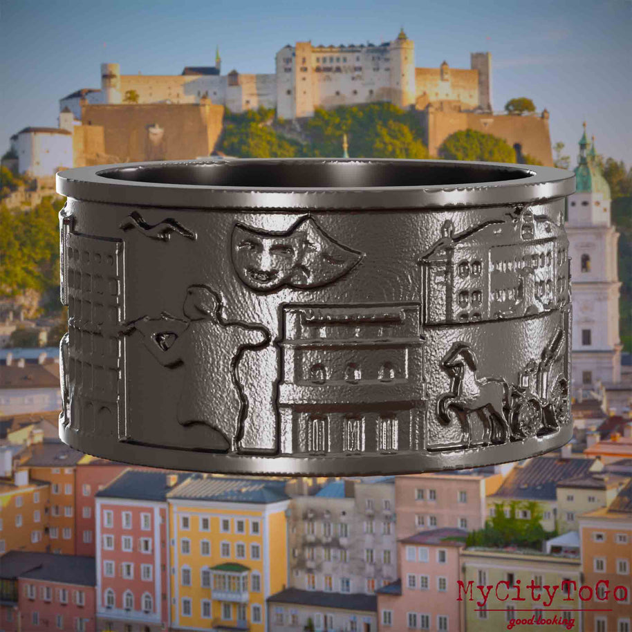 Ring aus Titan mit Reliefs bekannter Sehenswürdigkeiten der Stadt Salzburg. Den Hintergrund bildet eine Ansicht der Stadt Salzburg.