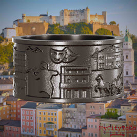 Ring aus Titan mit Reliefs bekannter Sehenswürdigkeiten der Stadt Salzburg. Den Hintergrund bildet eine Ansicht der Stadt Salzburg.