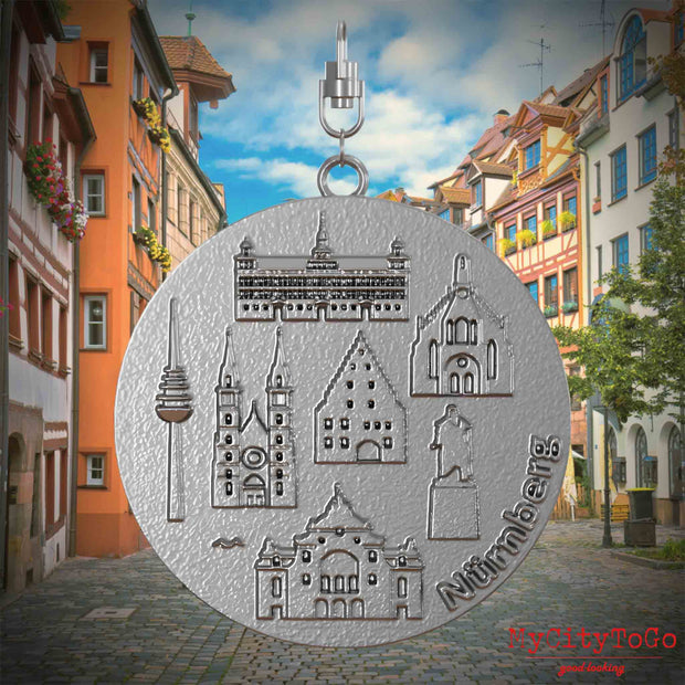 Halskette mit Drehwirbel und Vorderseite eines Schmuckanhängers aus Edelstahl, auf dem Reliefs bekannter Sehenswürdigkeiten der Stadt Nurnberg abgebildet sind. Den Hintergrund bildet eine Ansicht der Stadt Nuernberg.