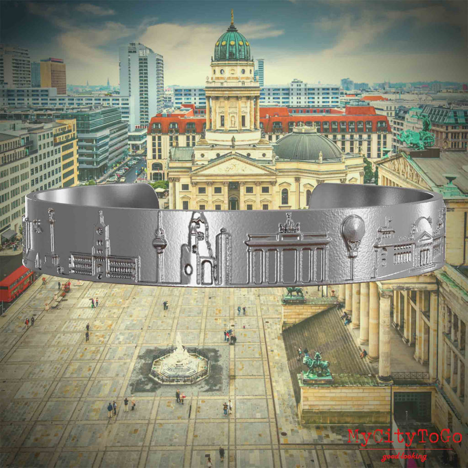 Armreif aus Edelstahl mit Reliefs bekannter Sehenswürdigkeiten der Stadt Berlin. Den Hintergrund bildet eine Ansicht der Stadt Berlin. 