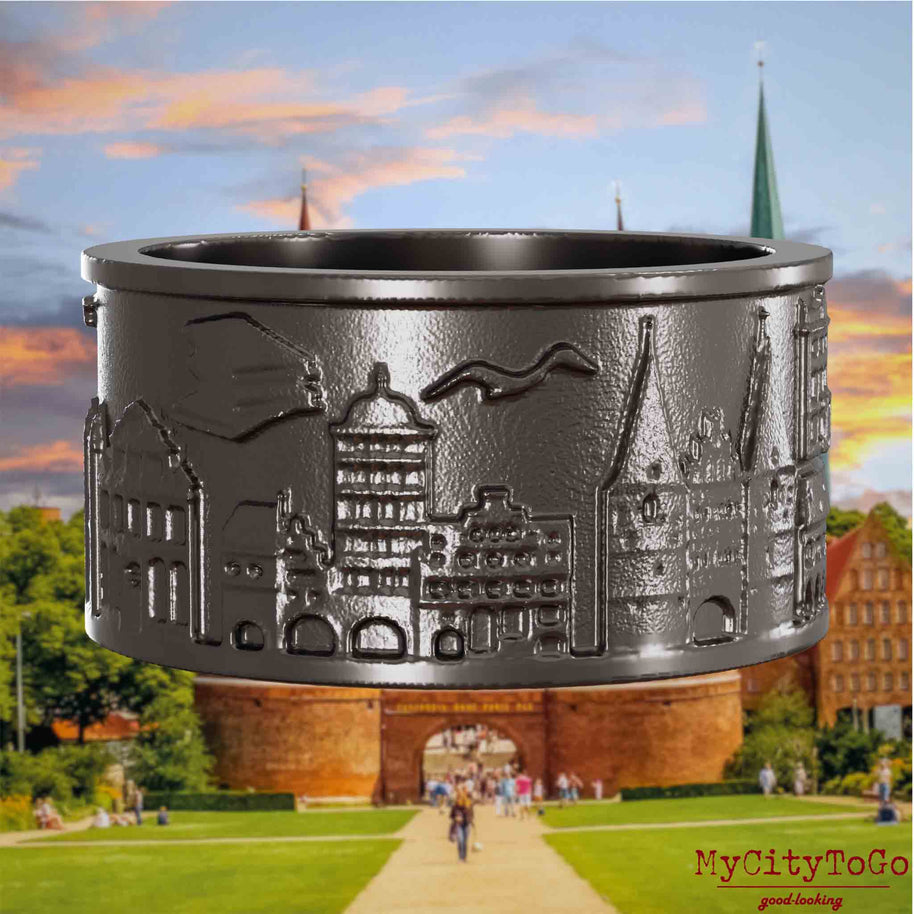 Ring aus Titan mit Reliefs bekannter Sehenswürdigkeiten der Stadt Luebeck. Den Hintergrund bildet eine Ansicht der Stadt Luebeck.