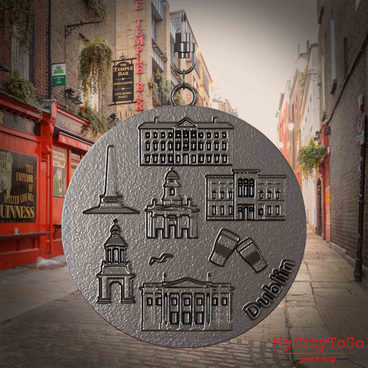 Halskette mit Drehwirbel und Vorderseite eines Schmuckanhängers aus Titan, auf dem Reliefs bekannter Sehenswürdigkeiten der Stadt Dublin abgebildet sind. Den Hintergrund bildet eine Ansicht der Stadt Dublin.
