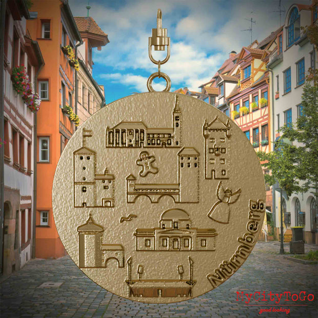 Halskette mit Drehwirbel und Vorderseite eines Schmuckanhängers aus vergoldetem Edelstahl, auf dem Reliefs bekannter Sehenswürdigkeiten der Stadt Nuernberg abgebildet sind. Den Hintergrund bildet eine Ansicht der Stadt Nuernberg.