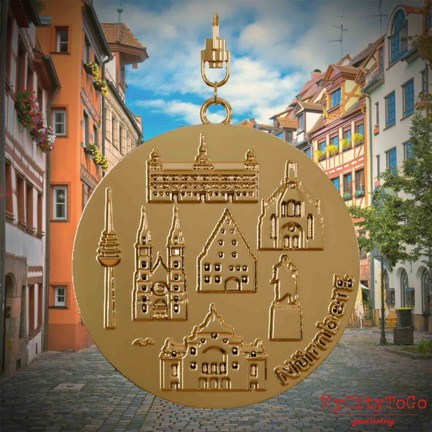 Halskette mit Drehwirbel und Vorderseite eines vergoldeten Schmuckanhängers, auf dem Reliefs bekannter Sehenswürdigkeiten der Stadt Nuernberg abgebildet sind. Den Hintergrund bildet eine Ansicht der Stadt Nuernberg.