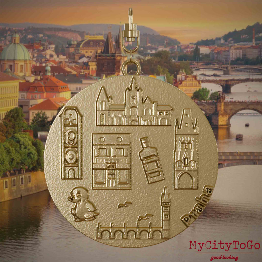 Halskette mit Drehwirbel und Vorderseite eines Schmuckanhängers aus vergoldetem Edelstahl, auf dem Reliefs bekannter Sehenswürdigkeiten der Stadt Prag abgebildet sind. Den Hintergrund bildet eine Ansicht der Stadt Prag.
