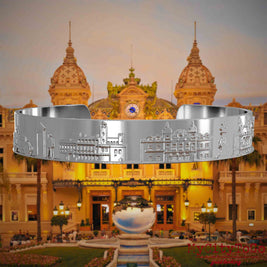 Versilberter Armreif mit Reliefs bekannter Sehenswürdigkeiten der Stadt Monte Carlo. Den Hintergrund bildet eine Ansicht der Stadt Monte Carlo.