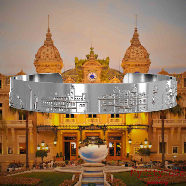 Versilberter Armreif mit Reliefs bekannter Sehenswürdigkeiten der Stadt Monte Carlo. Den Hintergrund bildet eine Ansicht der Stadt Monte Carlo.