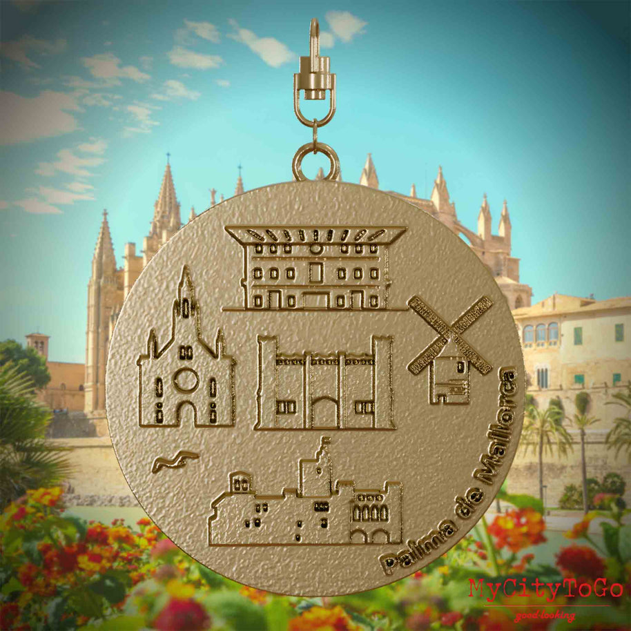Halskette mit Drehwirbel und Vorderseite eines Schmuckanhängers aus vergoldetem Edelstahl, auf dem Reliefs bekannter Sehenswürdigkeiten der Stadt Palma de Mallorca abgebildet sind. Den Hintergrund bildet eine Ansicht der Stadt Palma de Mallorca.
