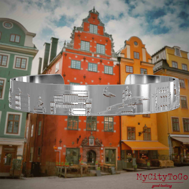 Versilberter Armreif mit Reliefs bekannter Sehenswürdigkeiten der Stadt Stockholm. Den Hintergrund bildet eine Ansicht der Stadt Stockholm.