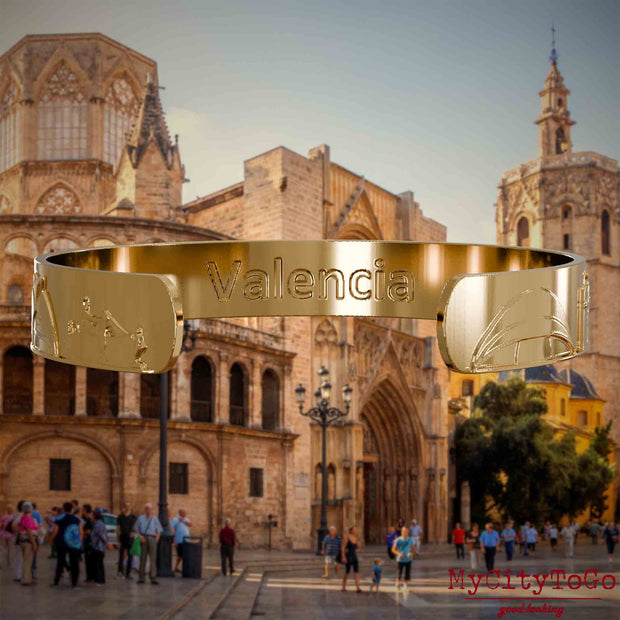 Innenseite eines vergoldeten Armreifs mit Reliefs bekannter Sehenswürdigkeiten der Stadt Valencia und einer Gravur des Stadtnamens. Den Hintergrund bildet eine Ansicht der Stadt Valencia.