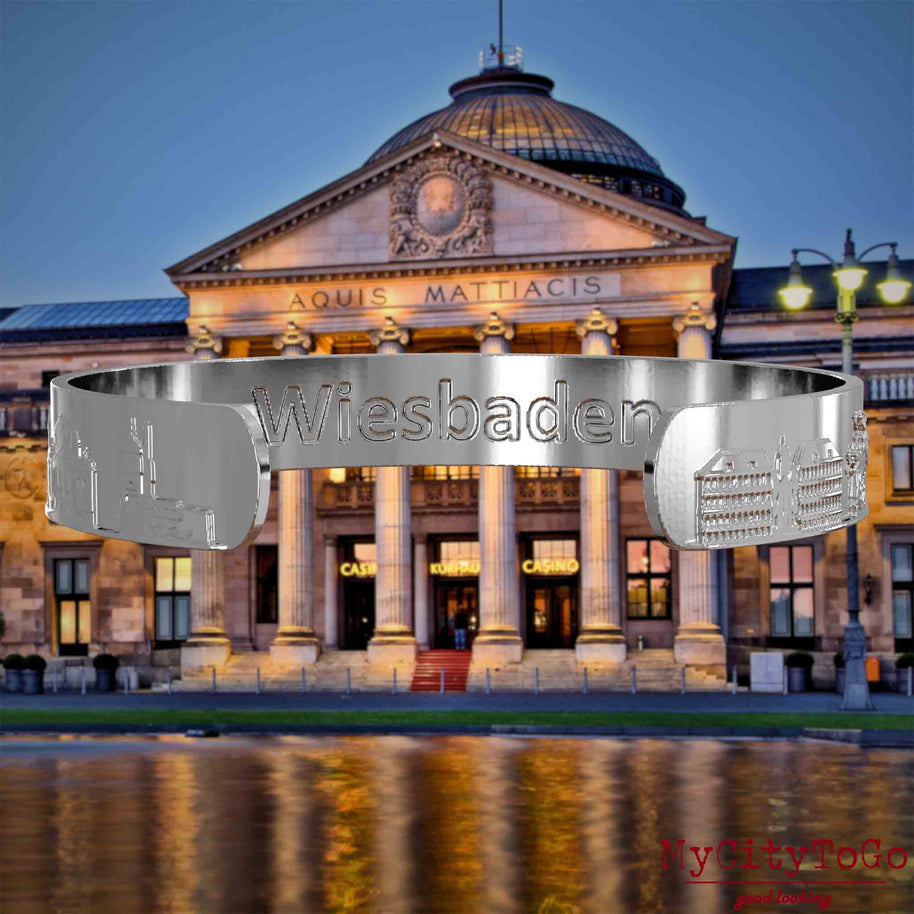 Interior of a silver bangle with reliefs of famous landmarks in the city of Wiesbaden and an engraving of the city's name. The background shows a view of the city of Wiesbaden.