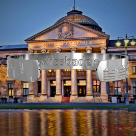 Interior of a silver bangle with reliefs of famous landmarks in the city of Wiesbaden and an engraving of the city's name. The background shows a view of the city of Wiesbaden.