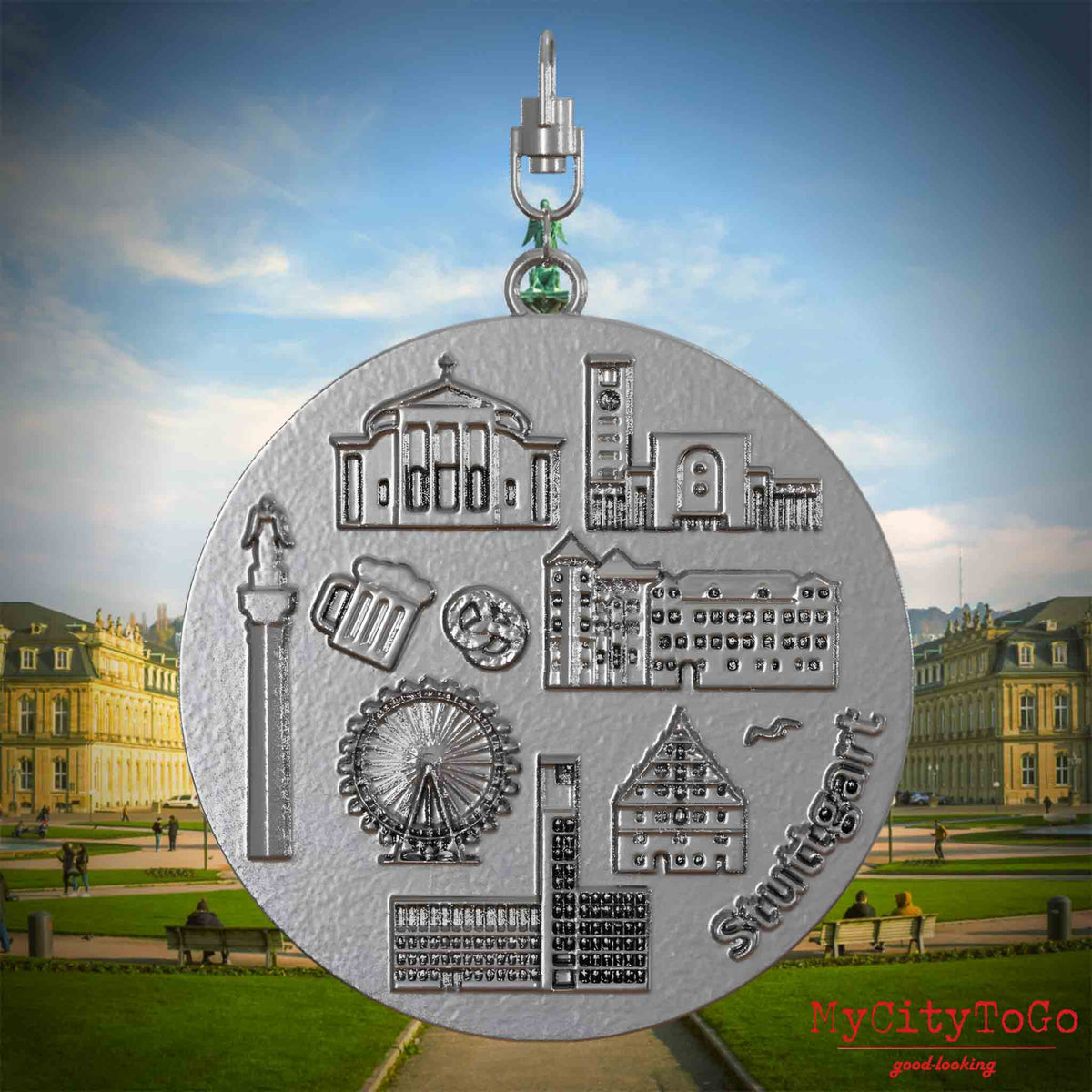 Halskette mit Drehwirbel und Rückseite eines Schmuckanhängers aus Edelstahl, auf dem Reliefs bekannter Sehenswürdigkeiten der Stadt Stuttgart abgebildet sind. Den Hintergrund bildet eine Ansicht der Stadt Stuttgart.
