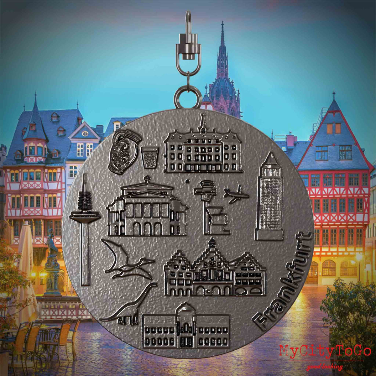 Halskette mit Drehwirbel und Rückseite eines Schmuckanhängers aus Titan, auf dem Reliefs bekannter Sehenswürdigkeiten der Stadt Frankfurt abgebildet sind. Den Hintergrund bildet eine Ansicht der Stadt Frankfurt.