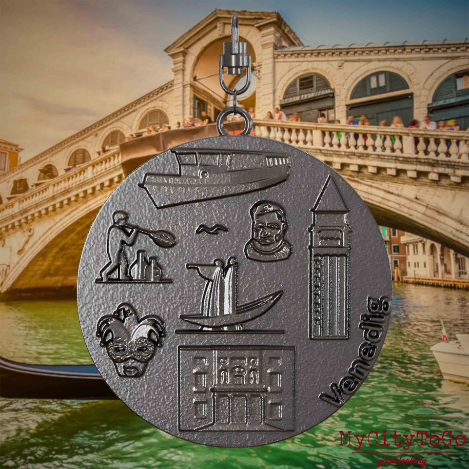 Halskette mit Drehwirbel und Rückseite eines Schmuckanhängers aus Titan, auf dem Reliefs bekannter Sehenswürdigkeiten der Stadt Venedig abgebildet sind. Den Hintergrund bildet eine Ansicht der Stadt Venedig.

