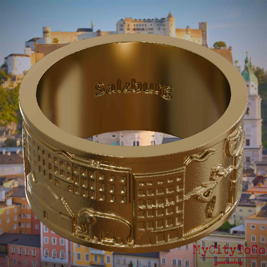 Ring aus vergoldetem Edelstahl mit Reliefs bekannter Sehenswürdigkeiten der Stadt Salzburg und einer Gravur des Stadtnamens auf der Innenseite. Den Hintergrund bildet eine Ansicht der Stadt Salzburg.