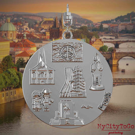 Halskette mit Drehwirbel und Rückseite eines silbernen Schmuckanhängers, auf dem Reliefs bekannter Sehenswürdigkeiten der Stadt Prag abgebildet sind. Den Hintergrund bildet eine Ansicht der Stadt Prag.
