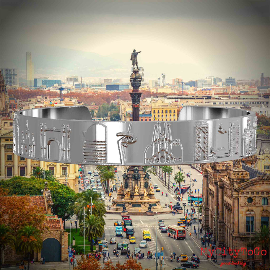 Versilberter Armreif mit Reliefs bekannter Sehenswürdigkeiten der Stadt Barcelona. Den Hintergrund bildet eine Ansicht der Stadt Barcelona.