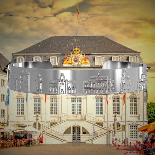 Versilberter Armreif mit Reliefs bekannter Sehenswürdigkeiten der Stadt Bonn. Den Hintergrund bildet eine Ansicht der Stadt Bonn.
