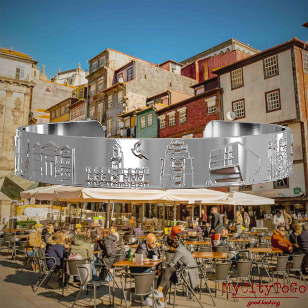 Versilberter Armreif mit Reliefs bekannter Sehenswürdigkeiten der Stadt Porto. Den Hintergrund bildet eine Ansicht der Stadt Porto.