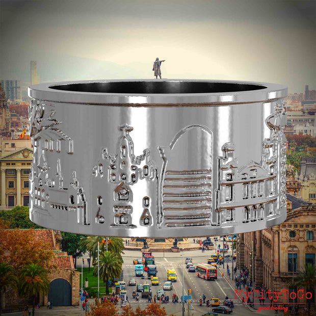 Silberner Ring mit Reliefs bekannter Sehenswürdigkeiten der Stadt Barcelona. Den Hintergrund bildet eine Ansicht der Stadt Barcelona.