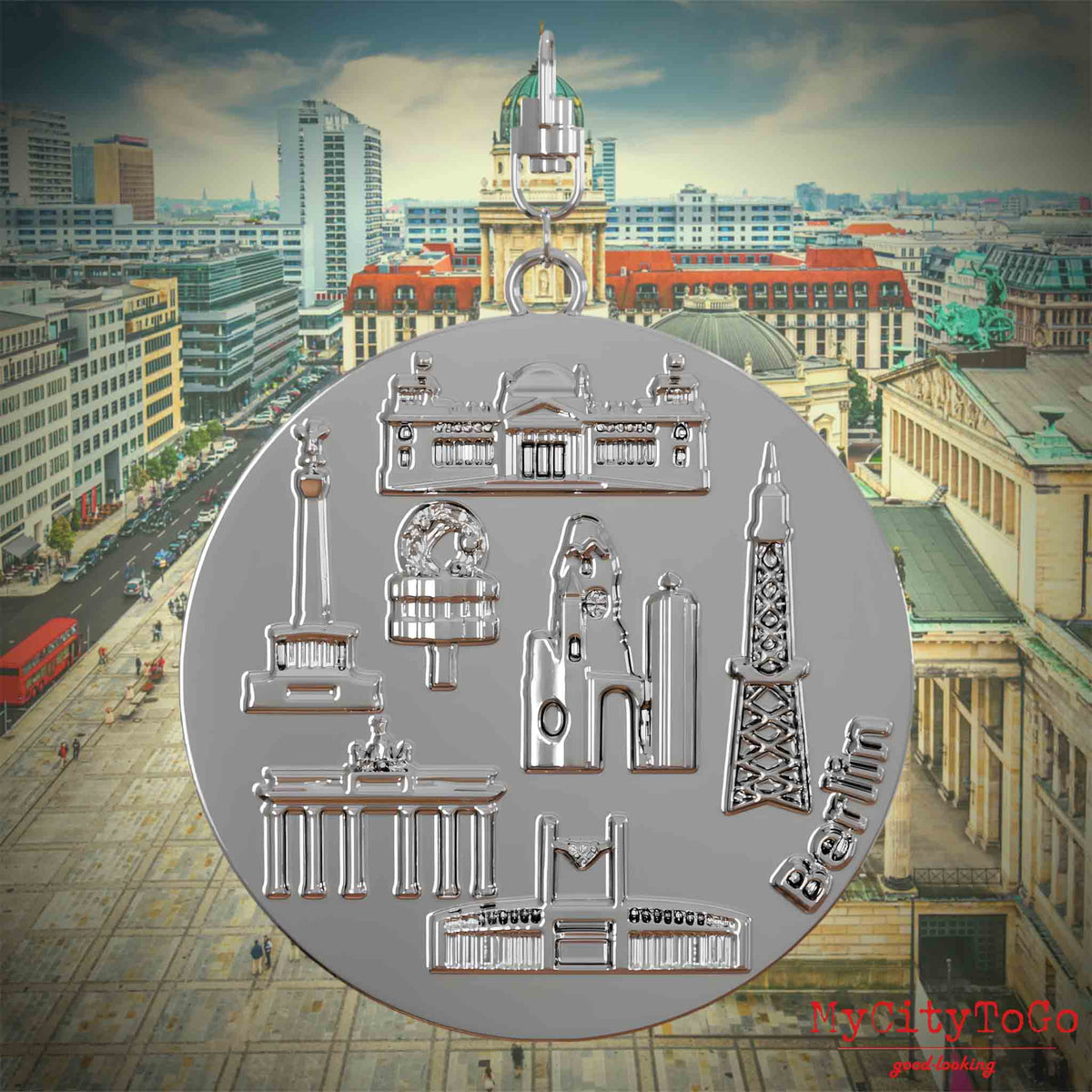 Halskette mit Drehwirbel und Rückseite eines silbernen Schmuckanhängers, auf dem Reliefs bekannter Sehenswürdigkeiten der Stadt Berlin abgebildet sind. Den Hintergrund bildet eine Ansicht der Stadt Berlin.