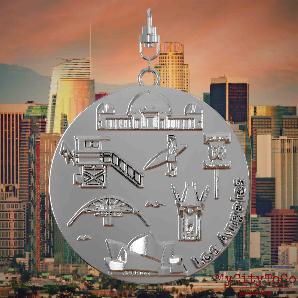 Halskette mit Drehwirbel und Rückseite eines silbernen Schmuckanhängers, auf dem Reliefs bekannter Sehenswürdigkeiten der Stadt Los Angeles abgebildet sind. Den Hintergrund bildet eine Ansicht der Stadt Los Angeles.
