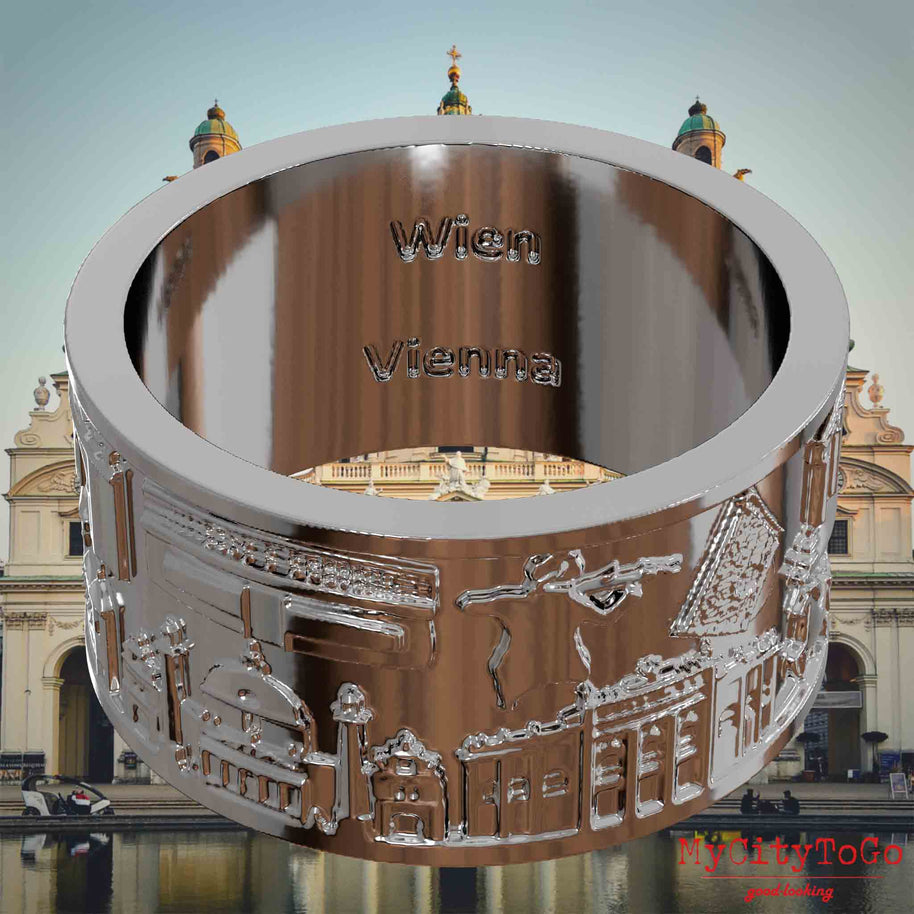 Versilberter Ring mit Reliefs bekannter Sehenswürdigkeiten der Stadt Wien und einer Gravur des Stadtnamens auf der Innenseite. Den Hintergrund bildet eine Ansicht der Stadt Wien.