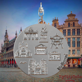 Halskette mit Drehwirbel und Rückseite eines silbernen Schmuckanhängers, auf dem Reliefs bekannter Sehenswürdigkeiten der Stadt Bruessel abgebildet sind. Den Hintergrund bildet eine Ansicht der Stadt Bruessel.
