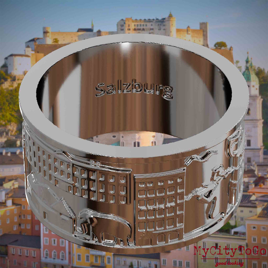 Versilberter Ring mit Reliefs bekannter Sehenswürdigkeiten der Stadt Salzburg und einer Gravur des Stadtnamens auf der Innenseite. Den Hintergrund bildet eine Ansicht der Stadt Salzburg.