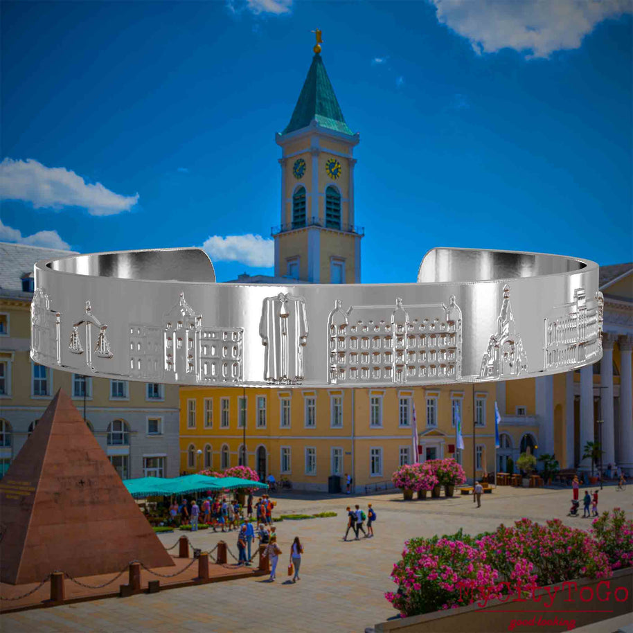 Versilberter Armreif mit Reliefs bekannter Sehenswürdigkeiten der Stadt Karlsruhe. Den Hintergrund bildet eine Ansicht der Stadt Karlsruhe.
