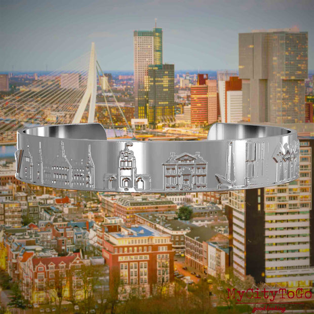 Versilberter Armreif mit Reliefs bekannter Sehenswürdigkeiten der Stadt Rotterdam. Den Hintergrund bildet eine Ansicht der Stadt Rotterdam.