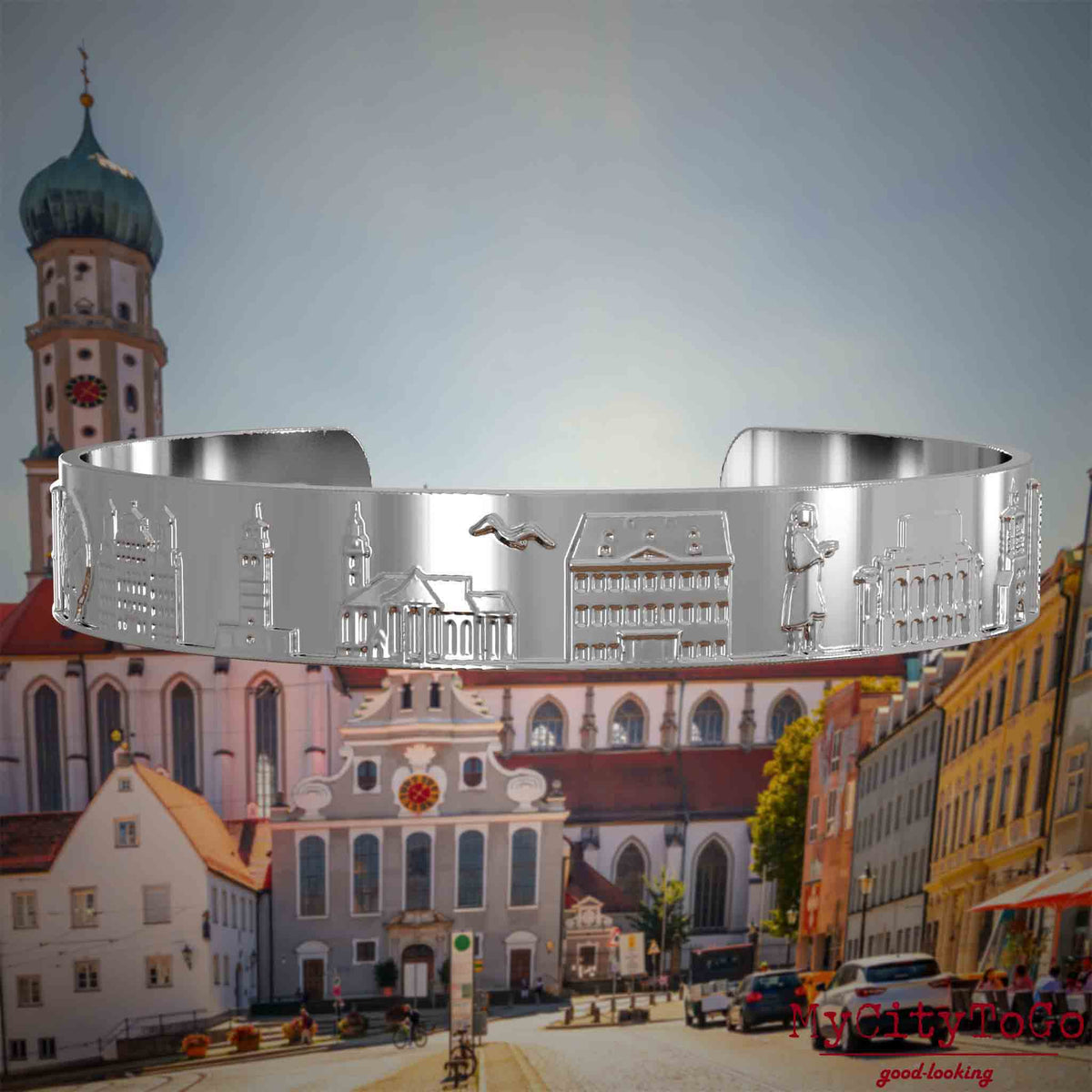 Versilberter Armreif mit Reliefs bekannter Sehenswürdigkeiten der Stadt Augsburg. Den Hintergrund bildet eine Ansicht der Stadt Augsburg.