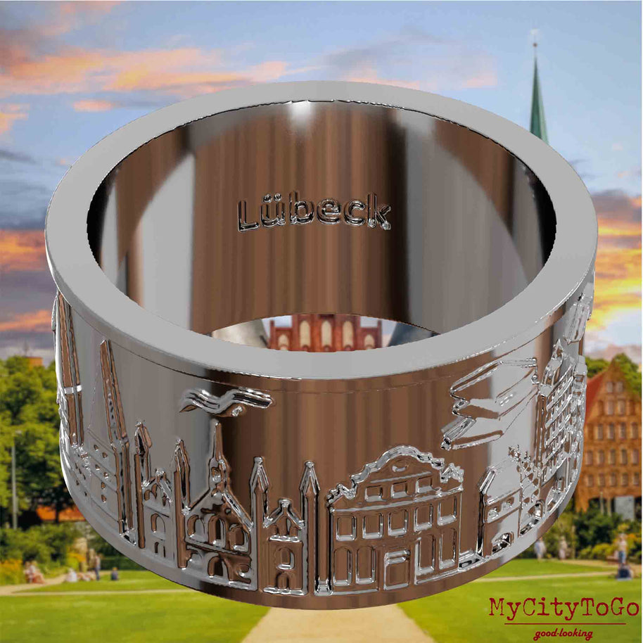 Versilberter Ring mit Reliefs bekannter Sehenswürdigkeiten der Stadt Luebeck und einer Gravur des Stadtnamens auf der Innenseite. Den Hintergrund bildet eine Ansicht der Stadt Luebeck.