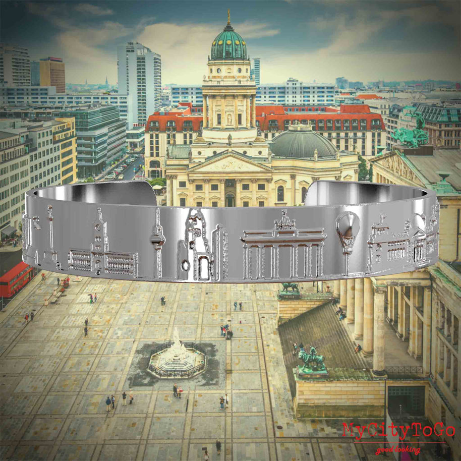 Silberner Armreif mit Reliefs bekannter Sehenswürdigkeiten der Stadt Berlin. Den Hintergrund bildet eine Ansicht der Stadt Berlin. 