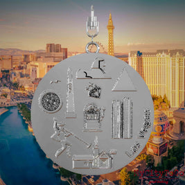 Necklace with swivel clasp and the front of a silver jewelry pendant featuring reliefs of famous Las Vegas landmarks. The background shows a view of the city of Las Vegas.