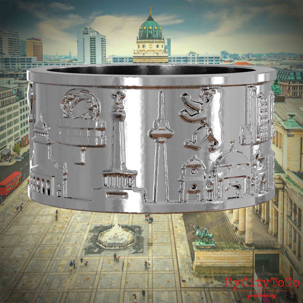 Silberner Ring mit Reliefs bekannter Sehenswürdigkeiten der Stadt Berlin. Den Hintergrund bildet eine Ansicht der Stadt Berlin.