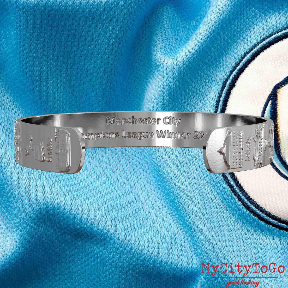 Innenseite eines silbernen Armreifs mit Reliefs der Stadien und Sehenswürdigkeiten der Spielorte während der Champions-League-Saison 22/23 von Manchester City und einer Gravur