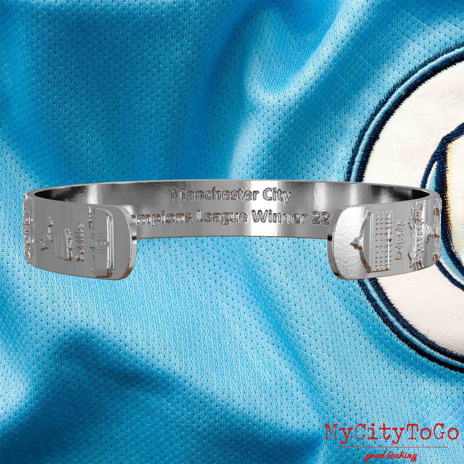 Innenseite eines silbernen Armreifs mit Reliefs der Stadien und Sehenswürdigkeiten der Spielorte während der Champions-League-Saison 22/23 von Manchester City und einer Gravur