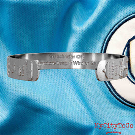 Innenseite eines silbernen Armreifs mit Reliefs der Stadien und Sehenswürdigkeiten der Spielorte während der Champions-League-Saison 22/23 von Manchester City und einer Gravur