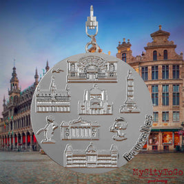 Halskette mit Drehwirbel und Vorderseite eines silbernen Schmuckanhängers, auf dem Reliefs bekannter Sehenswürdigkeiten der Stadt Bruessel abgebildet sind. Den Hintergrund bildet eine Ansicht der Stadt Bruessel.
