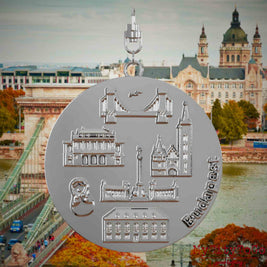 Halskette mit Drehwirbel und Vorderseite eines silbernen Schmuckanhängers, auf dem Reliefs bekannter Sehenswürdigkeiten der Stadt Budapest abgebildet sind. Den Hintergrund bildet eine Ansicht der Stadt Budapest.
