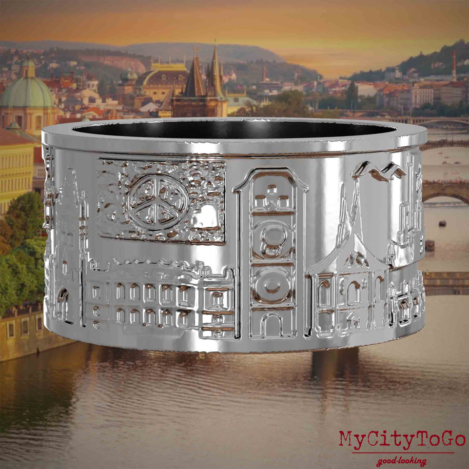 Silberner Ring mit Reliefs bekannter Sehenswürdigkeiten der Stadt Prag. Den Hintergrund bildet eine Ansicht der Stadt Prag.