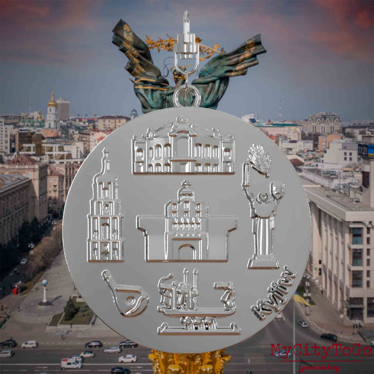 Halskette mit Drehwirbel und Vorderseite eines silbernen Schmuckanhängers, auf dem Reliefs bekannter Sehenswürdigkeiten der Stadt Kyjiw abgebildet sind. Den Hintergrund bildet eine Ansicht der Stadt Kyjiw.
