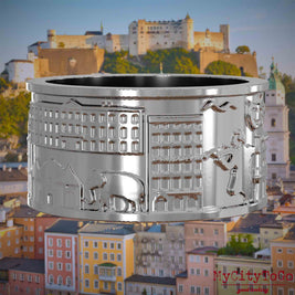 Silberner Ring mit Reliefs bekannter Sehenswürdigkeiten der Stadt Salzburg. Den Hintergrund bildet eine Ansicht der Stadt Salzburg.