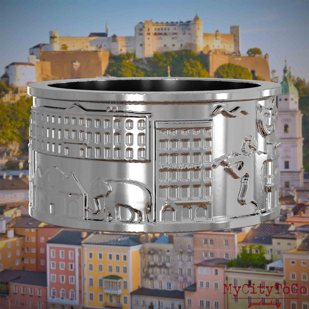 Silberner Ring mit Reliefs bekannter Sehenswürdigkeiten der Stadt Salzburg. Den Hintergrund bildet eine Ansicht der Stadt Salzburg.